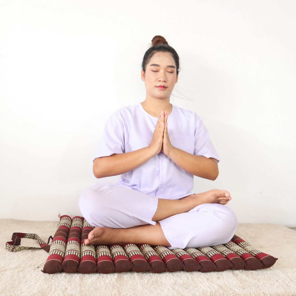 Woman meditating cross-legged on a red Thai zabuton meditation mat