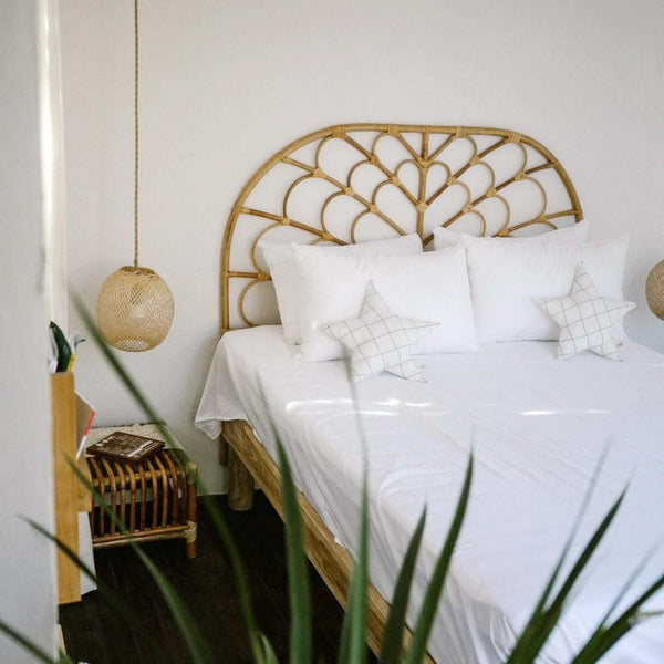 Round woven bamboo pendant light shade hanging beside a bed