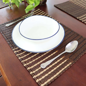 Set of white plates with blue rims on a woven placemat with silverware.