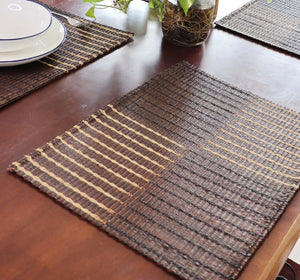 Woven placemat on a wooden table with a plant in the background