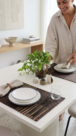 Woman setting a table with plates and cutlery in a bright room.