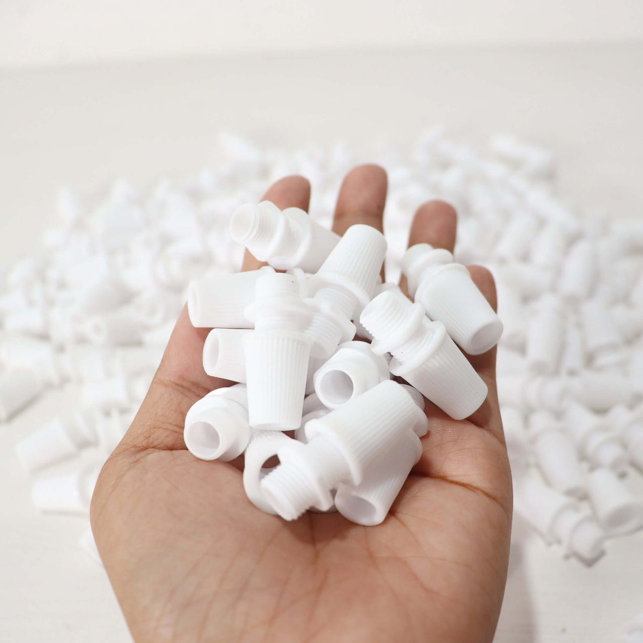 White Cord Grips Lampshade Holder – Plastic Screw Style Cord Grip (20 pcs.) held in hand with many around.