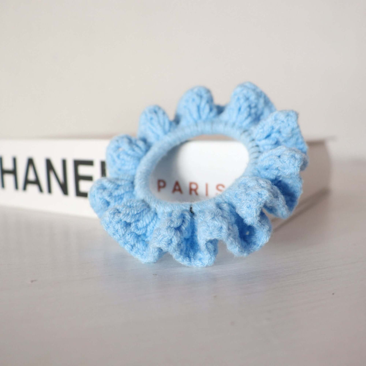 Purple Tones - Hand Crochet Scrunchies on a background of a designer brand box, showcasing a soft blue scrunchie.