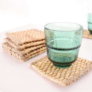 KA NOK PUN Water Hyacinth Boho Coaster Set of 4 with a glass on a rustic table.