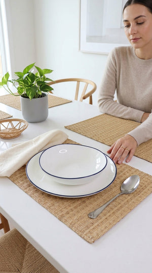 Woman sitting at a table with a set place setting and a plant in the background