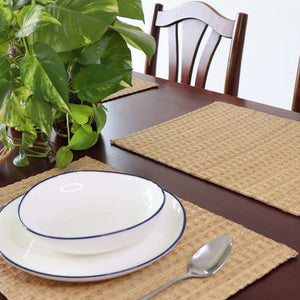 Dining table setting with plates, spoon, and placemats on a wooden table.