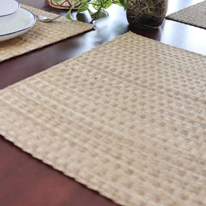 Woven placemat on a wooden table with a plant in the background