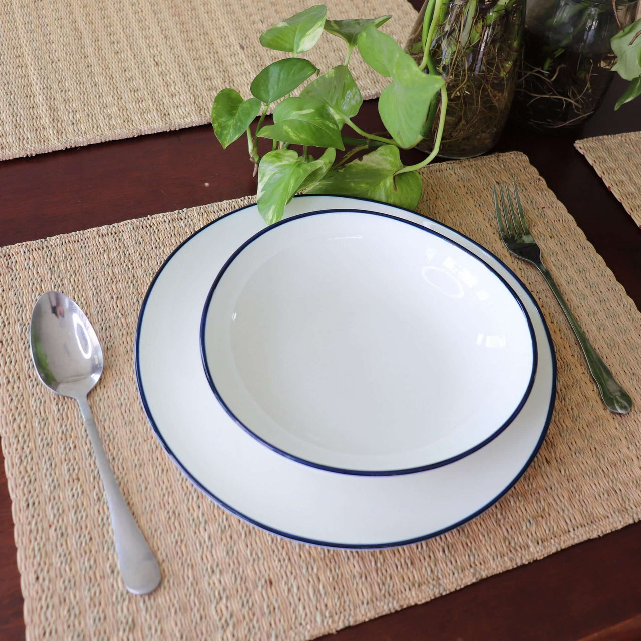 White bowl with blue rim on a woven placemat, accompanied by a spoon and fork.