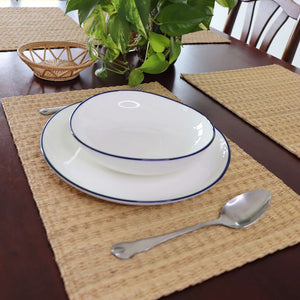 Set of white bowls with blue rims on a woven placemat with a spoon, on a wooden table.
