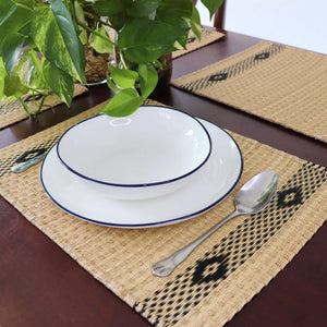 White plates with blue rims on a woven placemat with a spoon and plant in the background.