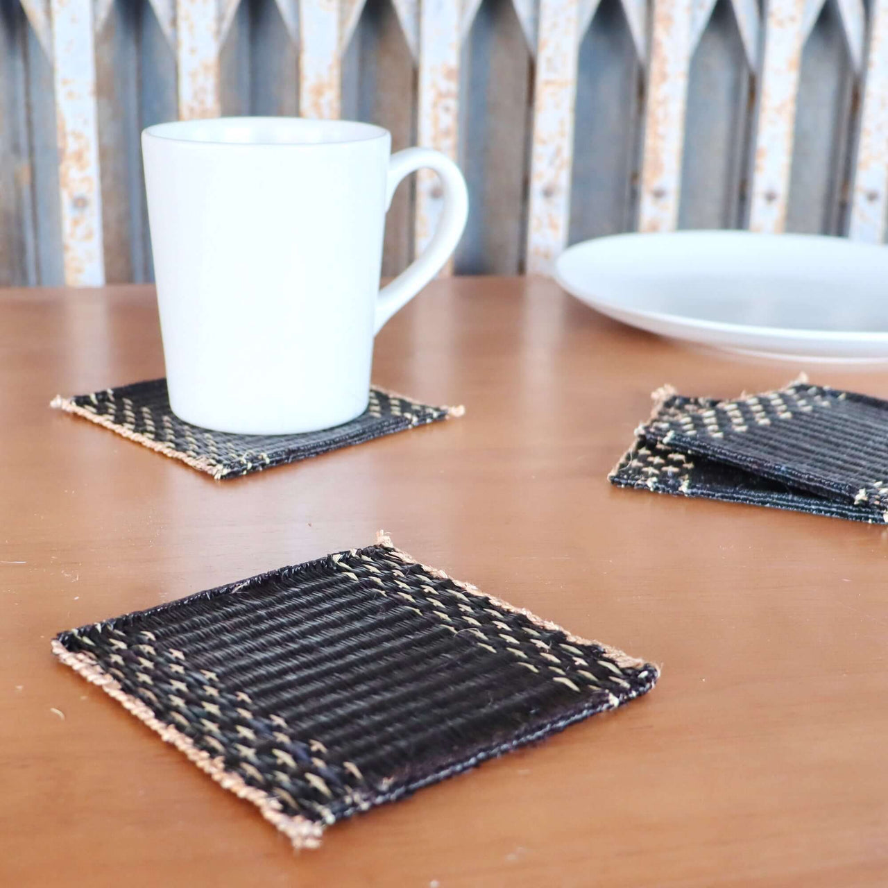 Lavila Handwoven Coaster Set of 4 with black woven centers and natural edges on a wooden table.