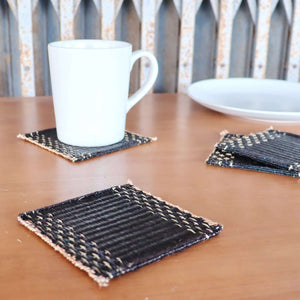 Lavila Handwoven Coaster Set of 4 with black woven centers and natural edges on a wooden table.
